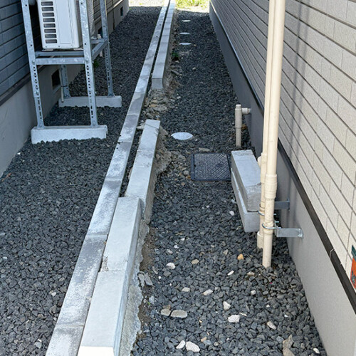 exleaf190927149 | エクスリーフのオフィシャルブログ Narrow gravel alley between two walls with exposed pipes and an outdoor unit mounted on a rack.