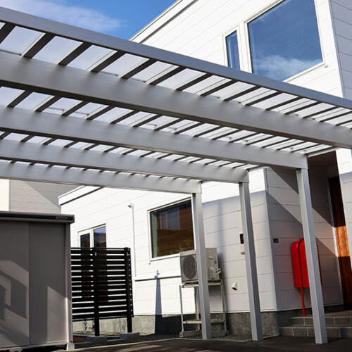 exleaf190927152 | エクスリーフのオフィシャルブログ Modern white house exterior with a gray metal pergola over a small patio, red mailbox by the entryway, and outdoor equipment nearby.