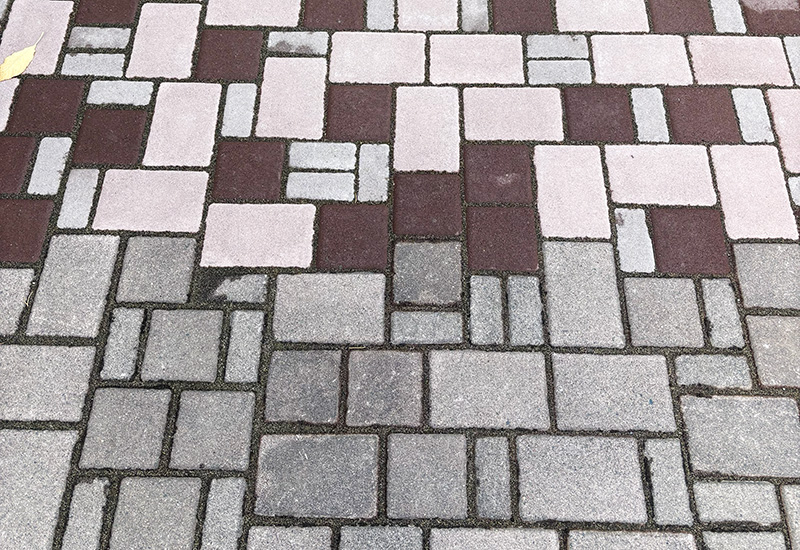 Close-up of a patterned walkway made of gray and burgundy rectangular paving stones.