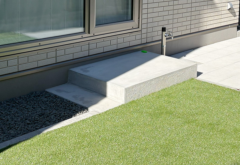 Concrete steps and landing beside a brick wall, with a small green object on the step and a faucet on the wall.