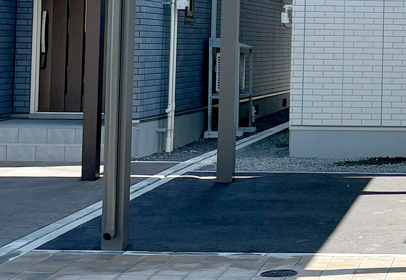 Entrance area of a modern building with metal posts casting shadows over a dark mat on light pavement.