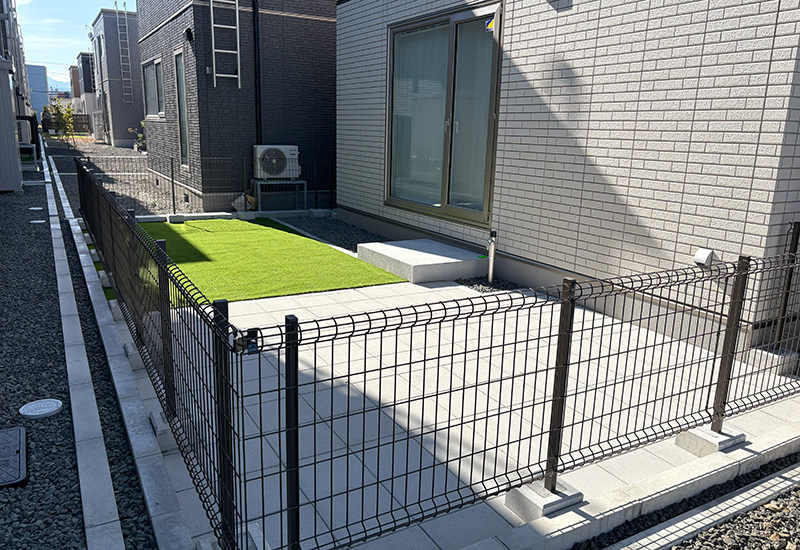 Fenced backyard of a townhouse: artificial grass patch, concrete patio, and sliding glass door on a gray brick wall.